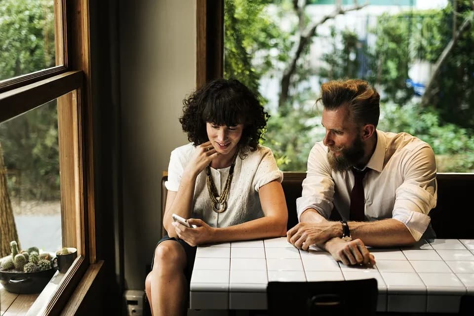 A man and woman sitting at a table looking at a phone
