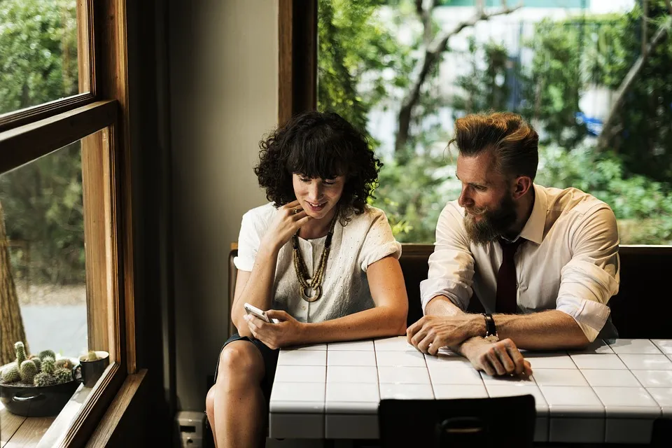 A man and woman sitting at a table looking at a phone